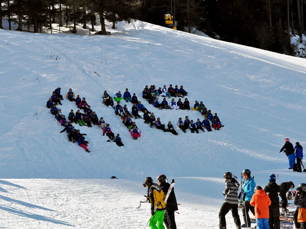 Große Gruppe formt im Schnee einen Schriftzug am Hang.